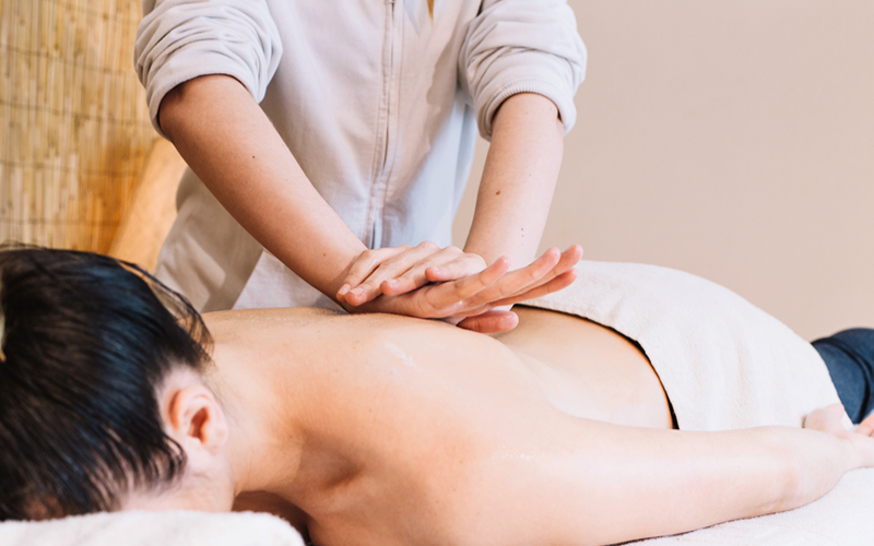 Therapist giving a back massage to relieve tech neck muscle tension.